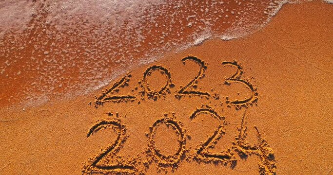Waves washing end of the year 2023 and beggining of new year 2024 handwriting text on beach sand