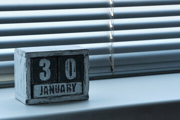 Morning January 30 on wooden calendar standing on window with blinds.