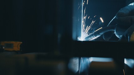 A man works with a welding machine at a factory - obrazy, fototapety, plakaty