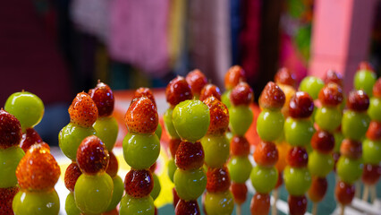 Pictures of sweet street food menus at temple fairs This menu is fruit skewers. It consists of large green grapes. and small strawberries skewered and drizzled with syrup. - obrazy, fototapety, plakaty