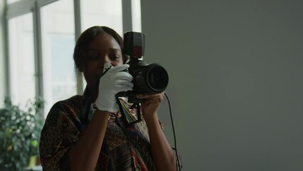Professional female photographer wearing white glove taking pictures with digital camera and telling model how to pose during shoot day in studio