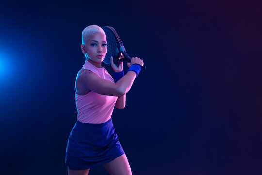 Padel tennis player with racket on tournament. Girl athlete with paddle racket on court with neon colors. Sport concept. Download a high quality photo for design of a sports app or tour events.