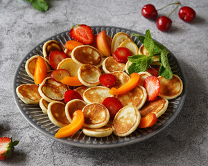mini pancakes decorated with fruit on a gray ceramic plate, daylight, close-up, no people