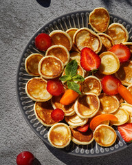 mini pancakes decorated with fruit on a gray ceramic plate, daylight, close-up, no people