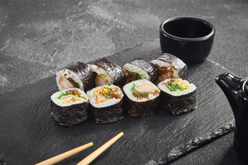 Authentic maki sushi rolls filled with tempura shrimp and wood ear mushrooms, served with soy sauce on a dark slate