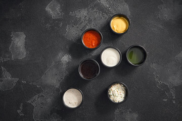 Obraz na płótnie Canvas A variety of dipping sauces presented in black ramekins against a textured dark backdrop, perfect for culinary accents