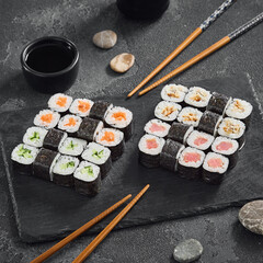 A classic assortment of hosomaki sushi featuring salmon, tuna, cucumber, and eel, beautifully arranged on a black slate with soy sauce.