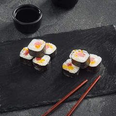  Delicate maki sushi rolls filled with fresh tuna and sweet mango, artfully displayed on a black slate with soy sauce on the side