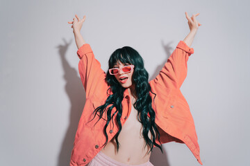 Cheeky emotional fashion young woman with long green color hair and trendy peach color lips, jacket and sunglasses dances on white background. Playful Hipster woman having fun. Color of the 2024 year. - obrazy, fototapety, plakaty