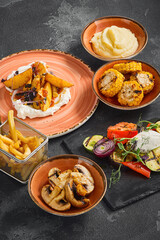 Assorted side dishes including grilled corn, mashed potatoes, potato wedges, grilled mushrooms, grilled vegetables, and French fries, artistically plated