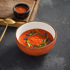 Classic chilled gazpacho tomato soup garnished with fresh herbs, served in a rustic bowl on a dark stone surface
