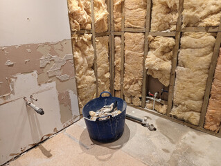 A bathroom renovation with the plumbing and insulation revealed in a stud wall.