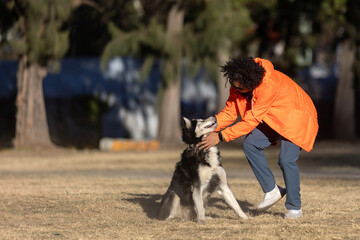 Mexican Latino man with curly hair, petting with his husky dog in a park