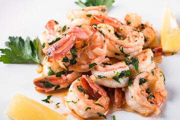 Fried Argentine shrimps with garlic and herbs on a white plate with lemon. 