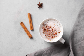 White mug of hot cocoa or chocolate with whipped cream, cinnamon sticks and star anise on a gray...