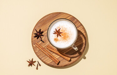 Fototapeta na wymiar Traditional Indian masala chai latte in a glass cup. Hot drink with milk, spices and herbs on a wooden board on a yellow background