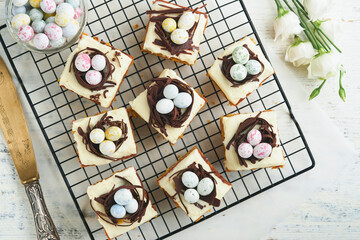 Easter carrot cake bars decorated with chocolate nest and chocolate candy eggs blossoming cherry or apple flowers on rustic light wooden backgrounds. Easter holiday meal. Traditional Easter food.