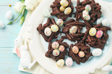 Easter chocolate nest cake with mini chocolate candy eggs with blossoming cherry or apple flowers on blue background table. Creative recipe for Easter table with holiday decorations. Top view.