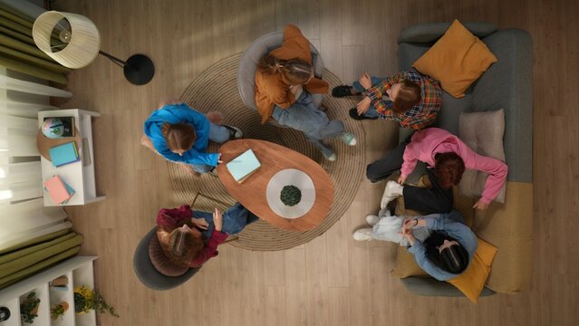 Top view of a group of students gathered at home in the living room. The teens are socializing sitting on a couch and chairs around a table. - Powered by Adobe