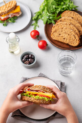 Hands holding a club sandwich with bacon, cheese, tomato and lettuce on a light background