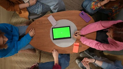 Top view of female students sitting at a coffee table with a tablet with a green screen in the center, close up. Advertising space, workplace.