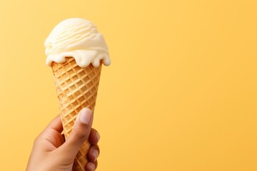 Hand holding vanilla milk ice cream cone on pastel background, a delightful summer treat