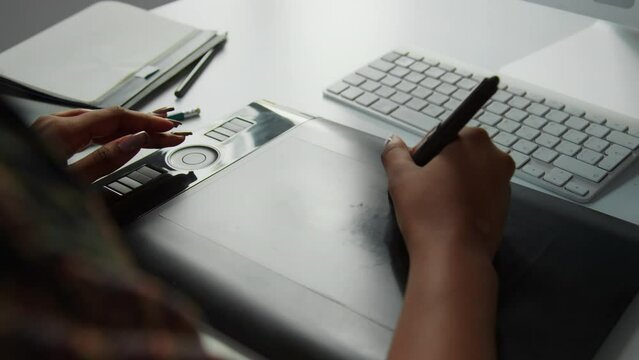 Close up shot of hands of unrecognizable woman drawing with stylus pen on graphic tablet at desk