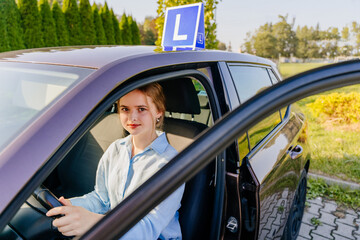 Young teen girl learning to drive a passenger car. A car with the letter L on the road. Driving school novice driver concept.