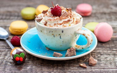 A beautiful blue cup of coffee with whipped cream, cocoa powder and raspberries on rustic wooden...