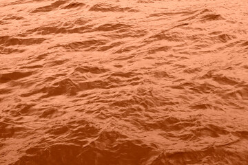 Peach Fuzz toned sea water texture. Pool water with sun reflections. Trendy colour 2024 year.