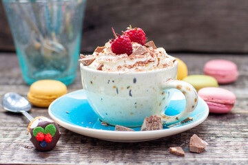 A beautiful blue cup of coffee with whipped cream, cocoa powder and raspberries on rustic wooden...