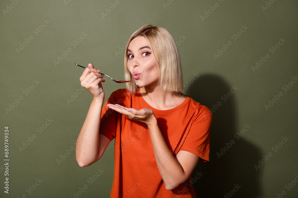 Sticker Photo of young blonde bob hair lady eat soup wear orange t shirt hold metal spoon blows hot meal tasting isolated on khaki color background