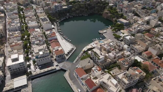 Aerial top view 4k footage by drone of Voulismeni lake and Agios Nikolaos city on Crete, camera soar over dense build area and small round lake.