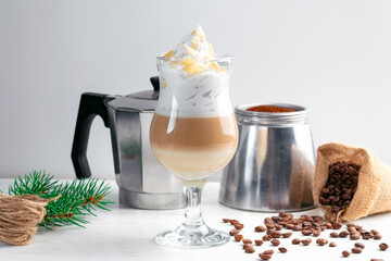 Cappuccino with whipped cream and almonds in a glass mug on a wooden table with coffee beans around
