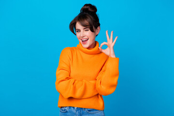 Photo of cheerful flirty lady wear knitted pullover winking showing okey sign isolated blue color background
