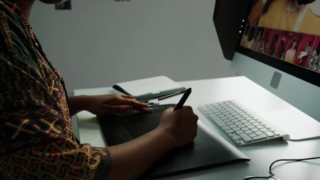 Tilt down shot of African American female photographer retouching image on computer with graphic tablet and stylus pen while working at desk in studio