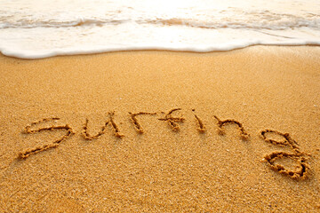 The word surfing written in the sand on the beach
