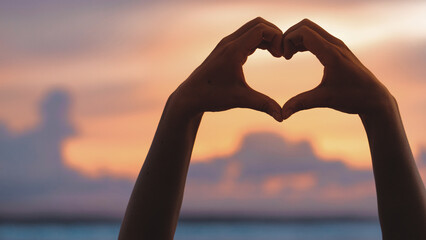Hands forming a heart shape with sunset silhouette