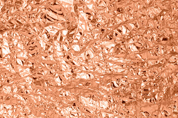 Background of crumpled metal foil. Color peach fuzz
