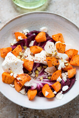 Salad with roasted sweet potato, radicchio, feta cheese and chopped pistachios in a beige plate, vertical shot, close-up