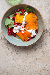 Rustic plate with persimmon, goat cheese, spinach and pomegranate salad, above view on a beige granite background, vertical shot, copy space