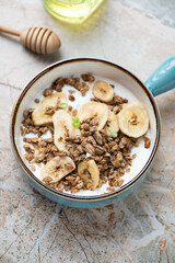 Turquoise serving bowl with yogurt, granola and banana chips, vertical shot on a pinkish granite background, selective focus