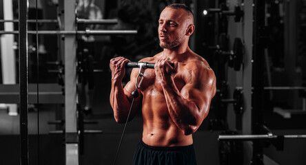 Fototapeta na wymiar Muscular bodybuilder doing bicep curls in cable crossover gym machine