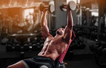 Muscular man doing bench press with heavy dumbbells for chest workout - obrazy, fototapety, plakaty