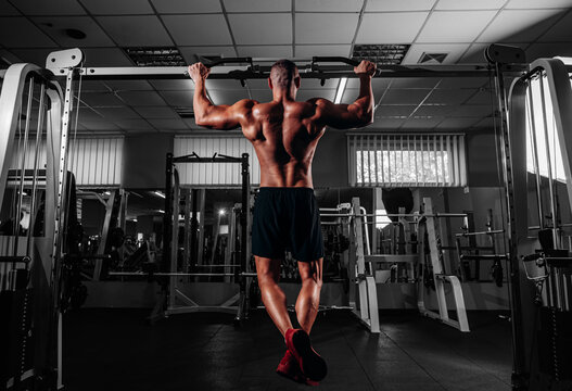 Back view of Muscular man doing pull up on horizontal bar in gym, working out. Strong fitness male pulling up, showing back