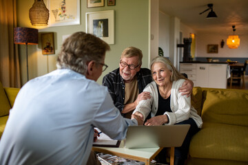 Happy senior couple shaking hands with therapist at home