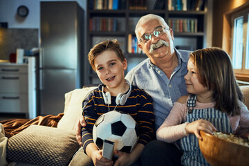 Happy grandfather watching tv at home with grandchildren