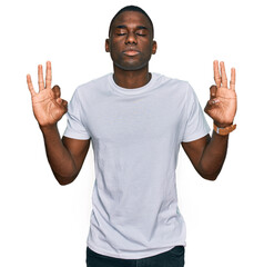 Fototapeta premium Young african american man wearing casual white t shirt relaxed and smiling with eyes closed doing meditation gesture with fingers. yoga concept.