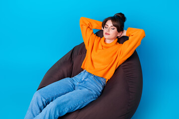 Photo of shiny dreamy lady wear knitted pullover sitting bean bag arms behind head closed eyes isolated blue color background