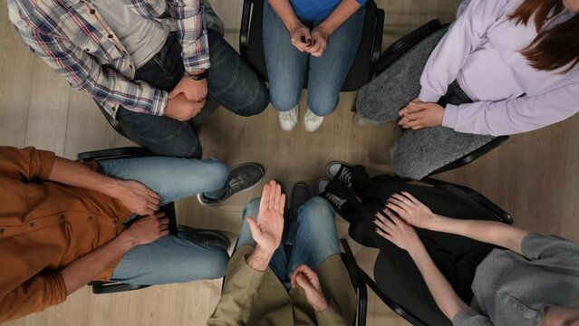 Close up of a group of people sitting in a circle in the frame above. They have come for a therapy session with a psychologist, they are socializing, working through problems, supporting each other